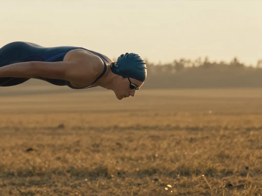a swimmer before the plunge in a racing suit in a coy glance from under lowered lashes, in a backlit golden-hour field,
